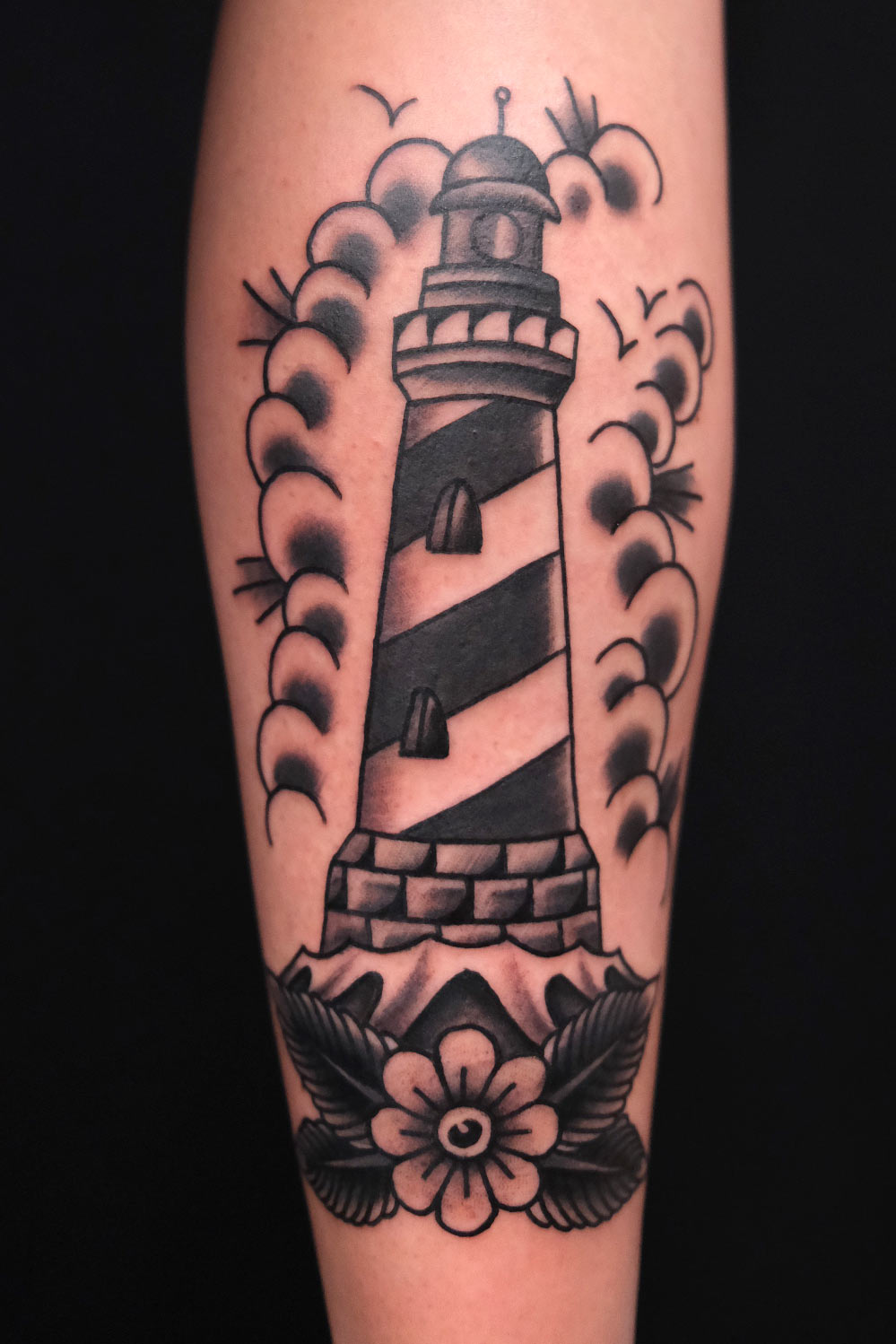 Tattoo in Schwarz-Grau mit Leuchtturm, Blüte und Wolken – gestochen bei Good Old Times Tattoo in Berlin Mitte.