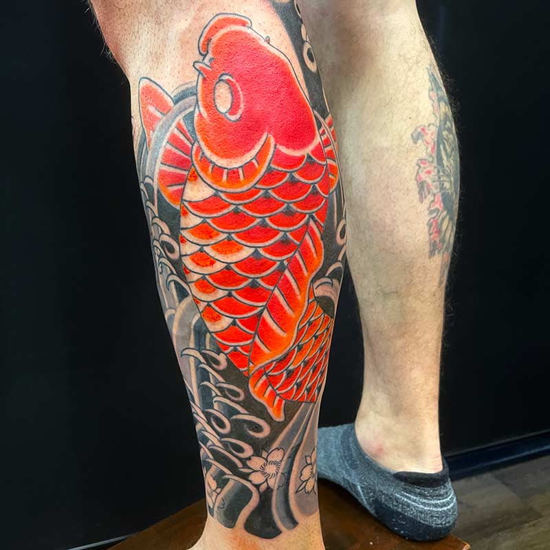 Traditionelles Koi-Tattoo auf der Wade: Ein roter Karpfen schwimmt flussaufwärts, begleitet von Kirschblüten – ein klassisches Motiv aus der japanischen Irezumi-Kunst, das Neuanfang, Ausdauer und Lebensfreude symbolisiert.